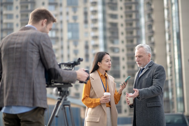 Reporter donna che indossa un abito beige che fa domande a un uomo dai capelli grigi