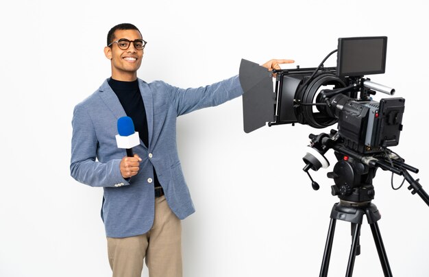 Reporter uomo afroamericano in possesso di un microfono e riferire notizie su muro bianco isolato che punta il dito verso il lato e presentare un prodotto