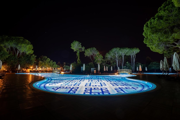 Resort turistico di lusso con sedie a sdraio vuote e ombrelloni ripiegati accanto a una scintillante piscina illuminata