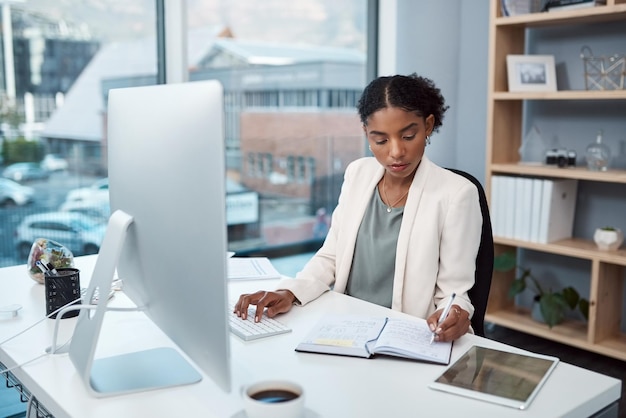 Responsabile finanziario che scrive note digitando sulla tastiera di un computer e pianificando di controllare i dati finanziari in ufficio Capo serio pensando di organizzare le scadenze fiscali o di programmare riunioni di lavoro nel taccuino