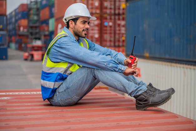 Responsabile logistico che parla sul walkietalkie al magazzino di container per il controllo dei container di carico nella spedizione del terminal dell'iarda di container.