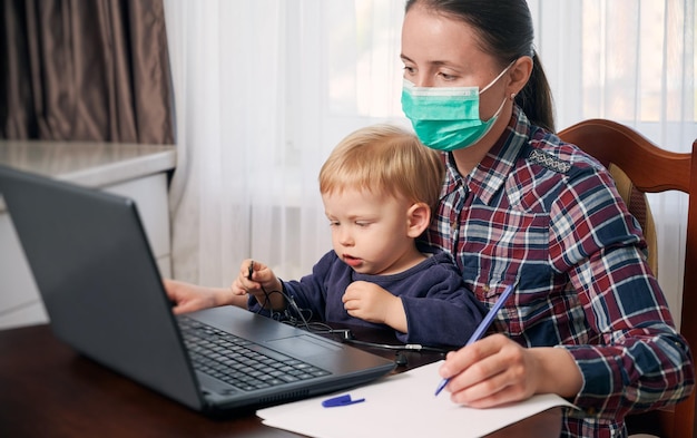 Resta a casa madre in una maschera che lavora a distanza mentre si prende cura del suo bambino Le moderne tecnologie aiutano a mantenere il lavoro Messa a fuoco selettiva