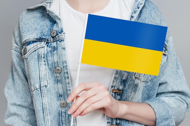Resta con l'Ucraina La mano di una donna tiene una piccola bandiera dell'Ucraina isolata su uno sfondo grigio in studio Vittoria del Giorno dell'Indipendenza Relazioni politiche