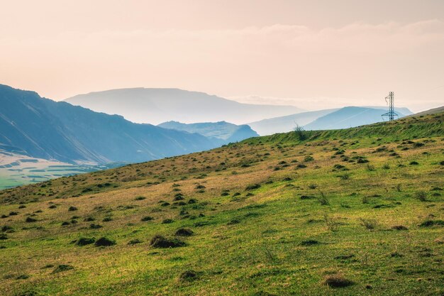 Rete di fili e pali del telegrafo sulle colline di montagna. Paesaggio atmosferico con sagome di montagne sullo sfondo del cielo rosa dell'alba. Tramonto in toni sbiaditi.