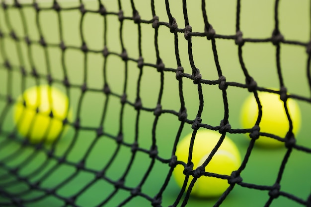 rete di tennis in campo verde, sfocato tre palline in background