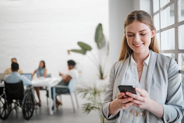 Rete telefonica e comunicazione con una donna d'affari sui social media in un ufficio per un incontro con un team in background Marketing pubblicitario e lavoro di squadra con un lavoratore che digita un messaggio