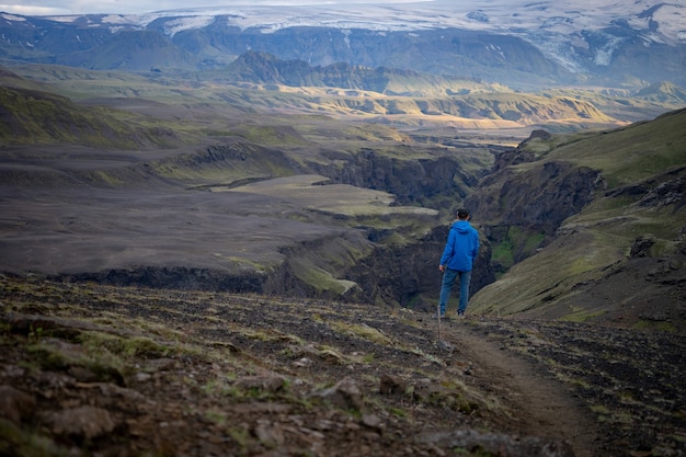 Retro della giacca da portare dell'uomo caucasico alto che sta sopra la montagna innevata sulla pista di Laugavegur, Islanda. Promuovere uno stile di vita sano.