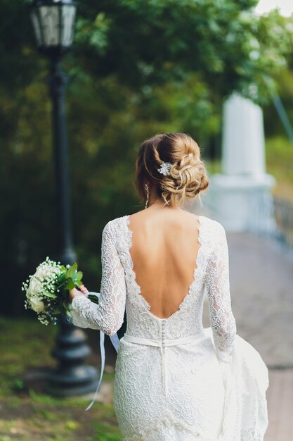 retro della sposa in abito bianco che tiene un mazzo di rose