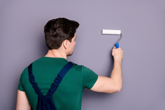 Retro foto sul lato posteriore di concentrato operaio vernice copia spazio utilizzando bianco spazzola a rullo desidera rinnovare il suo appartamento indossare t-shirt verde uniforme isolato su grigio muro di colore