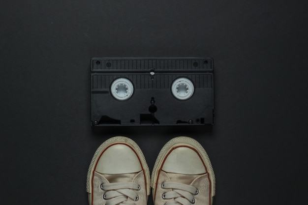 Retro vecchie scarpe da ginnastica e videocassetta su sfondo nero. anni 80. Vista dall'alto