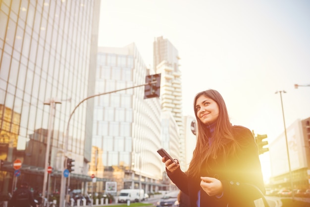 Retroilluminazione esterna della giovane bella donna di affari facendo uso dello smartphone