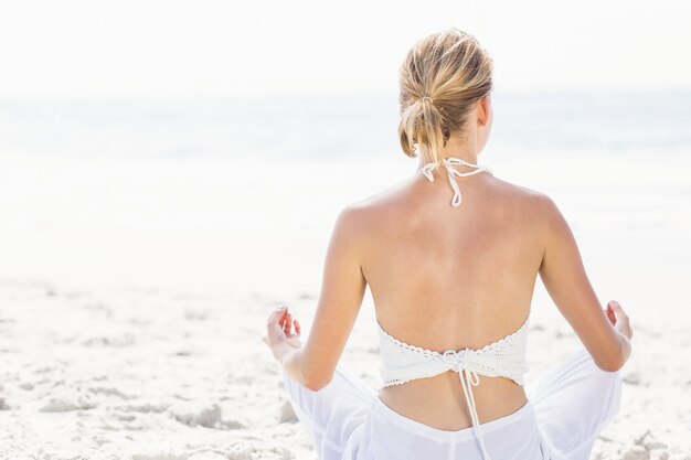 Retrovisione della donna che esegue yoga sulla spiaggia