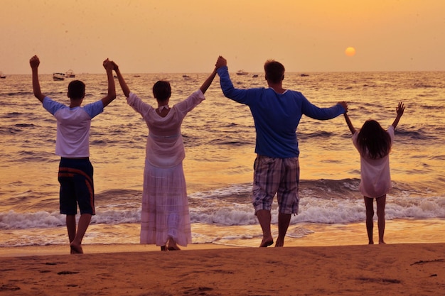 Retrovisione della famiglia che sta sulla spiaggia sabbiosa e che si tiene per mano insieme