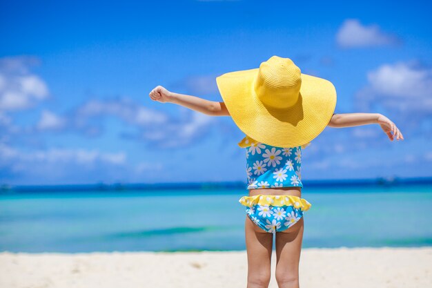 Retrovisione della neonata in grande cappello che esamina il mare sulla spiaggia di sabbia bianca