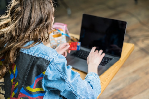 Retrovisione di una carta di debito della tenuta della donna e di per mezzo del computer portatile per la compera online