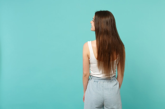 Retrovisione posteriore di giovane donna attraente in abiti casual leggeri che guardano da parte isolato su sfondo blu muro turchese in studio. Persone sincere emozioni, concetto di stile di vita. Mock up copia spazio.