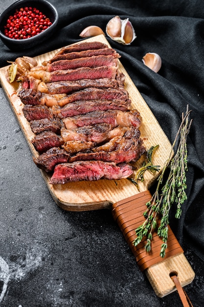 Rib eye alla griglia, bistecca alla ribey su un tagliere, mediamente cotta. carne marmorizzata. sfondo nero. vista dall'alto