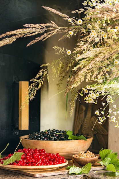 Ribes rosso e nero in piastre. Ricco raccolto di frutti di bosco. Accanto alle bacche sono un bouquet di erbe di campo e margherite. Verticale. Posto per il testo