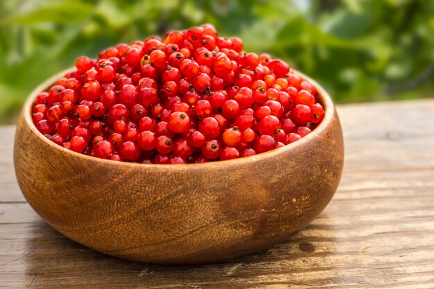 Ribes rosso in un piatto di legno su un tavolo in giardino. Copia spazio