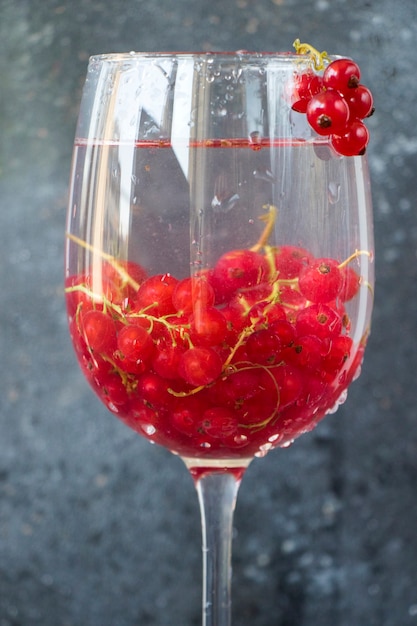 Ribes rosso nel bicchiere di vino sullo sfondo grigio e blu. Grande gruppo di bacche colorate.