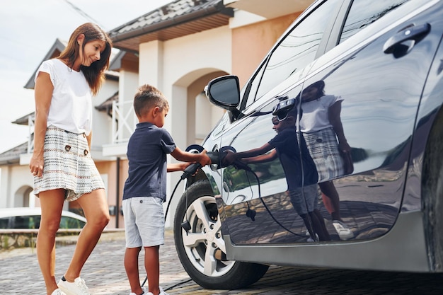 Ricarica dell'auto Donna con ragazzino vicino all'automobile moderna durante il giorno