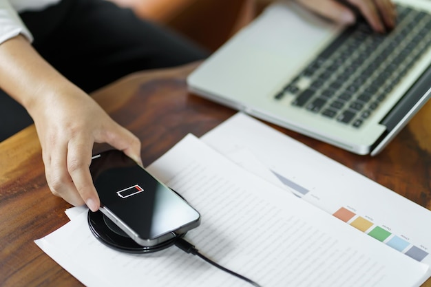 Ricarica della batteria del telefono cellulare con il dispositivo di ricarica wireless sul tavolo Ricarica dello smartphone su un tappetino di ricarica Telefono cellulare vicino al caricabatterie wireless Concetto di tecnologia di stile di vita moderno