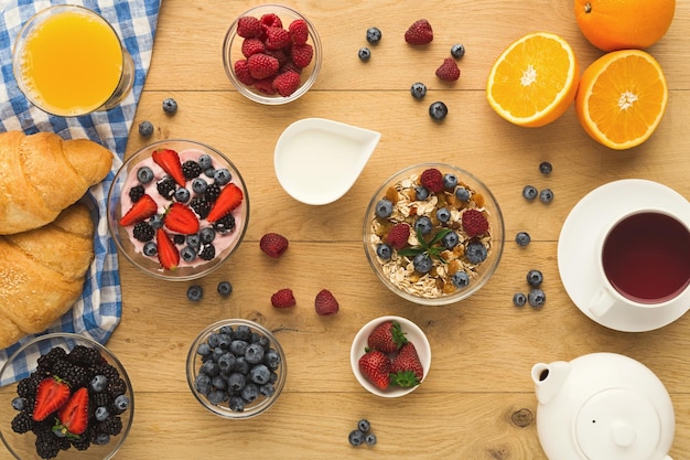 Ricca colazione continentale. Croissant francesi, muesli, yogurt, vasetto di latte, teiera, tazza di caffè nero caldo e tanti frutti di bosco per gustosi pasti mattutini. Delizioso inizio di giornata, vista dall'alto