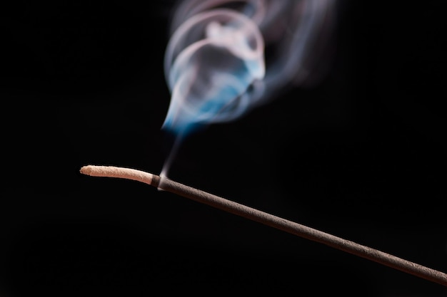 Riccioli di fumo dal bastoncino di incenso che brucia per il relax e la meditazione su sfondo nero