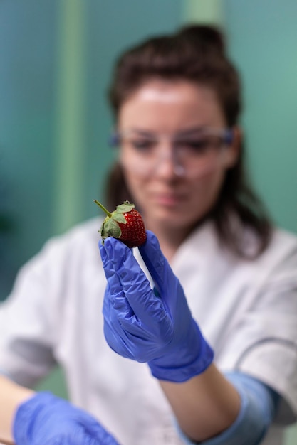 Ricercatore biologo in possesso di fragole organiche che analizzano dopo l'iniezione di liquido antiparassitario che lavora all'esperimento di frutti ogm nel laboratorio ospedaliero di microbiologia. Frutta geneticamente modificata