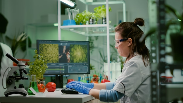 Ricercatore donna scienziato digitando competenze biochimiche sul computer per esperimento di microbiologia. Equipe medica che lavora in un laboratorio farmaceutico analizzando la mutazione genetica