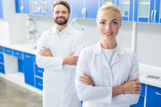 Ricercatore femminile. Felice bella donna bionda in piedi con le mani incrociate e ti guarda mentre si trova in laboratorio