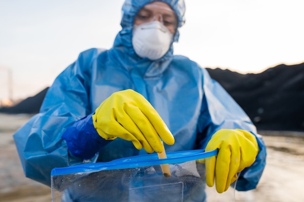 Ricercatore o ecologista contemporaneo in conalls protettivi che mettono nel pacchetto un pallone con un campione di acqua sporca proveniente da un'area pericolosa