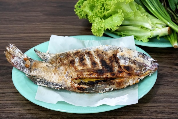 Ricetta tailandese di pesce alla griglia con verdure fresche su fondo di legno.