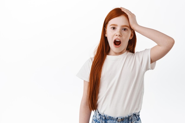 Ricorda dimenticare. Carina bambina rossa, bambino con lunghi capelli rossi e lentiggini dimenticato, tenendo la mano sulla testa e dire ahi, sbattere contro qualcosa, sfondo bianco