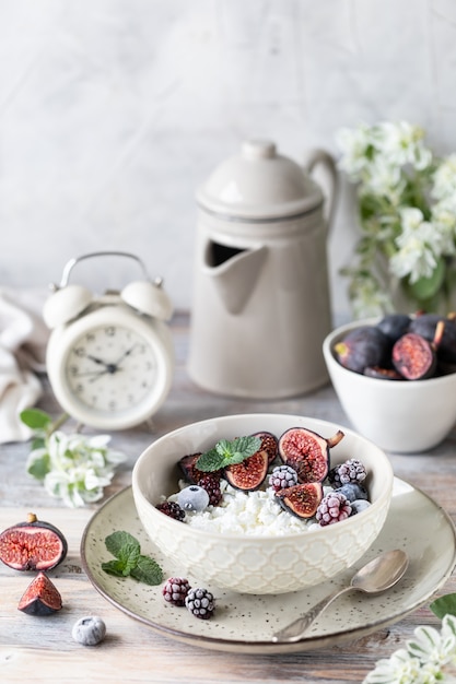 Ricotta con fichi, bacche, miele. Tazza di caffè e caffettiera. Prima colazione. Tavolo di legno.