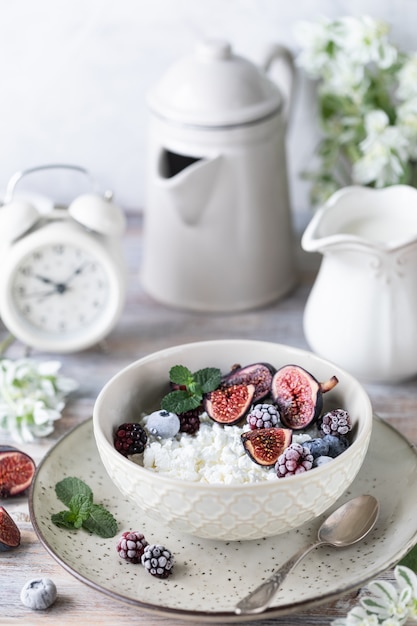 Ricotta con fichi, bacche, miele. Tazza di caffè e caffettiera. Prima colazione. Tavolo di legno.