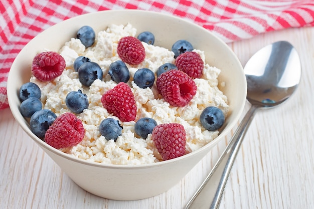 Ricotta con lamponi e mirtilli in una ciotola su fondo di legno bianco