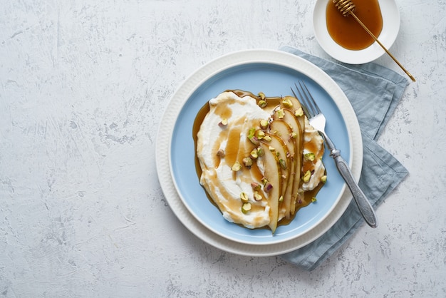 Ricotta con pere, pistacchi e miele o sciroppo d'acero sulla zolla blu sul tavolo bianco.