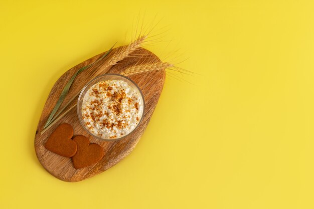 Ricotta cosparsa di briciole di biscotti, biscotti con cannella a forma di cuore, spighe di grano su una tavola di legno su superficie gialla