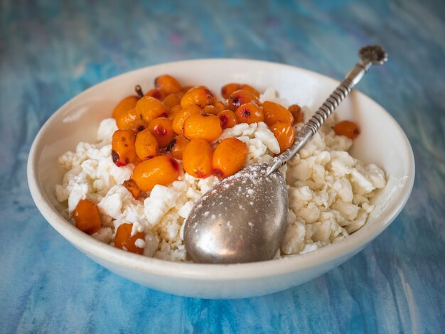 Ricotta e bacche di olivello spinoso appena congelate per una colazione dietetica leggera su una carta blu na