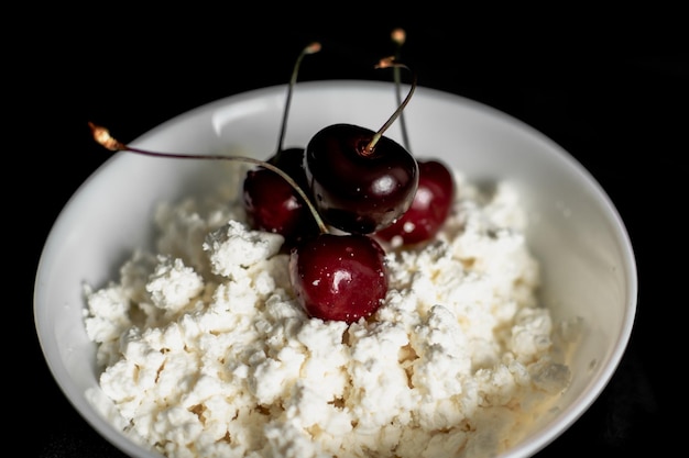 ricotta fatta in casa con ciliegie mature in un piatto bianco su sfondo nero