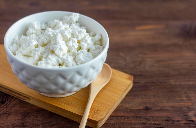 Ricotta fatta in casa in una ciotola bianca su uno sfondo di legno.