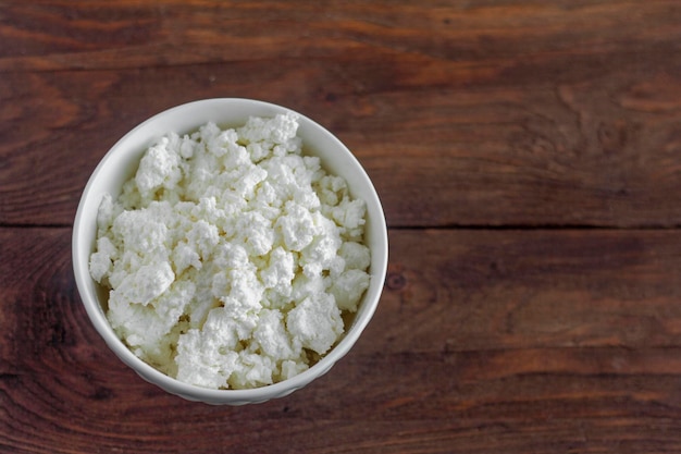 Ricotta fatta in casa in una ciotola bianca su uno sfondo di legno.