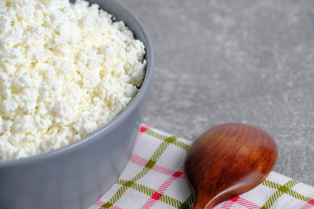 Ricotta fatta in casa in una ciotola di vetro con un asciugamano a scacchi sullo sfondo di un cucchiaio di legno