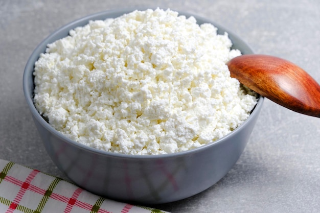 Ricotta fatta in casa in una ciotola di vetro con un asciugamano a scacchi sullo sfondo di un cucchiaio di legno