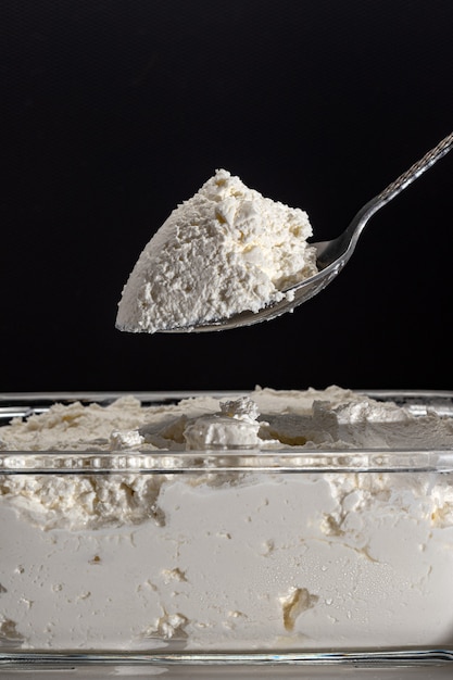 Ricotta fresca in contenitore di vetro e cucchiaio. cagliata isolata