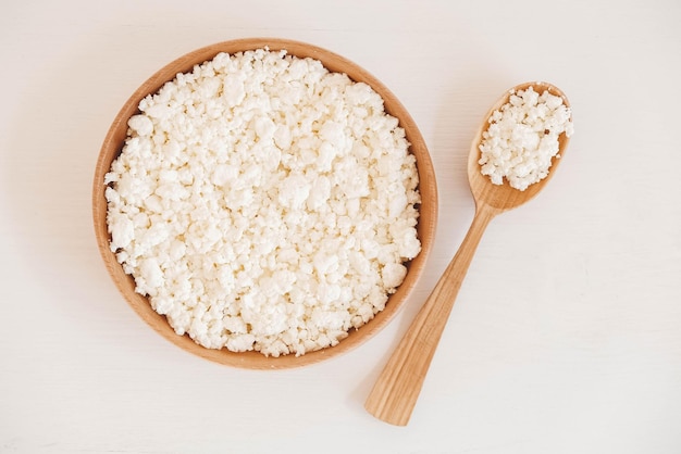 Ricotta in un piatto di legno con un cucchiaio su sfondo bianco