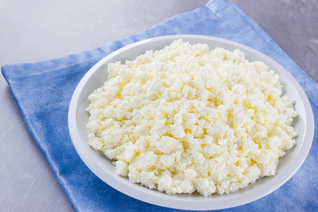 Ricotta in un piatto. Ricotta fresca in zolla bianca. Formaggio a pasta molle su un tovagliolo blu