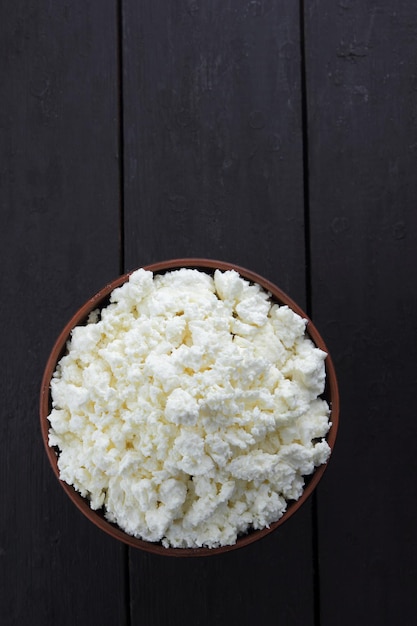 Ricotta in una ciotola di argilla su uno sfondo di legno nero Primo piano di cibi sani per la colazione