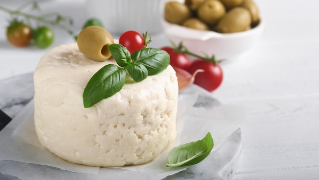 Ricotta Ricotta fatta in casa con basilico aglio pomodori e olive verdi su pergamena brossura e stand su vecchie piastrelle beige sfondo Cibo italiano Messa a fuoco selettiva